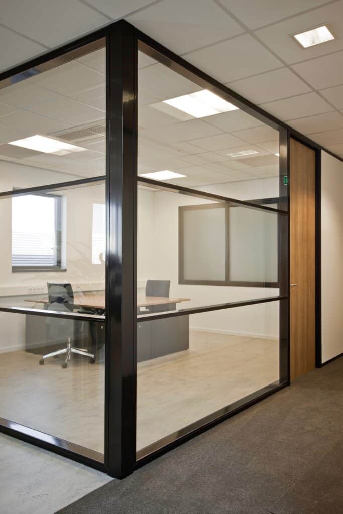 Glazen scheidingswand in een kantooromgeving met bureau en stoelen.