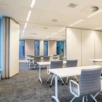 Modern klaslokaal met witte tafels, grijze stoelen en een flexibele paneelwand.