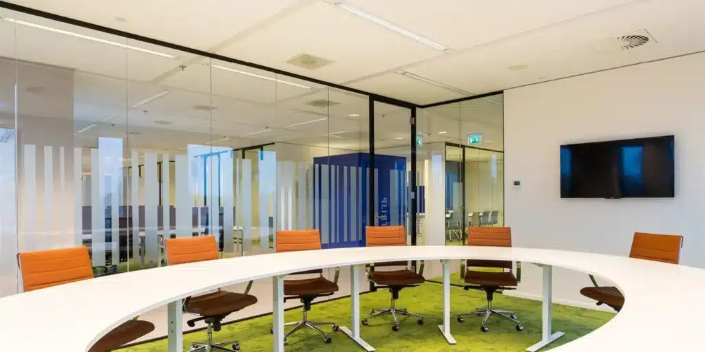 Moderne vergaderruimte met ovale tafel en oranje stoelen.