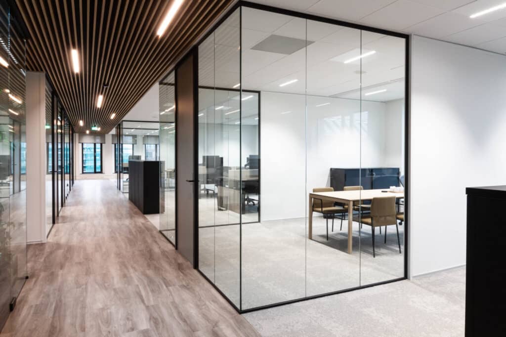 Moderne vergaderruimte met glazen wanden, een houten plafond en een lichte vergadertafel in een kantoorpand.
