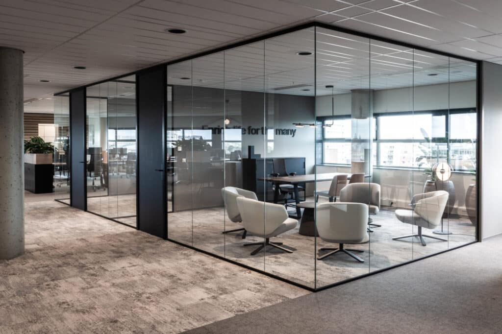 Moderne vergaderruimte afgescheiden door glazen kantoorwanden met comfortabele grijze stoelen in een kantooromgeving.